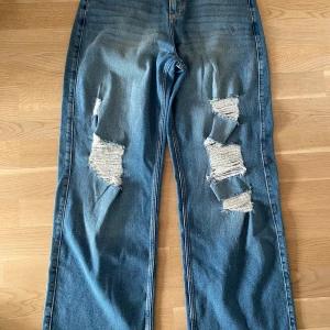 Hollister high-rise baggy jeans blå - Säljer ett par blå high-rise vintage baggy jeans från Hollister med rejält slitna detaljer och stora hål på båda benen. Jeansen har en loose passform och är tillverkade i stretchigt denim för extra komfort.