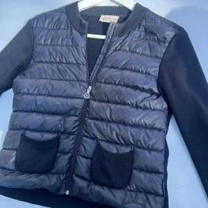 Svart cardigan från Moncler - Snygg svart pufferjacka från Moncler med quiltad framsida, ribbade muddar och två stickade fickor. Jackan har dragkedja med Moncler-logga och långärmade ärmar i mjukt material. Skriv om frågor💞💞jackan är i storlek xs men passar S