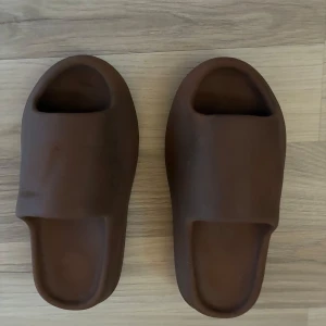 Bruna chunky slides med räfflad sula - Säljer ett par bruna slides med chunky, räfflad sula och öppen tå. De är tillverkade i syntetmaterial och har en clean, minimalistisk look. Perfekta för chill dagar eller när du vill ha något bekvämt och stilrent på fötterna.storlek 42 men passar mycket mindre