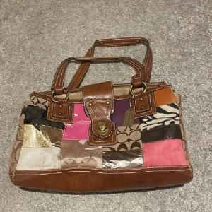 Patchwork handväska från Coach - Unik handväska från Coach i patchwork-stil med bruna skinnhandtag och detaljer. Väskan har inslag av rosa, lila, guld, beige och zebramönster i olika material som skinn, mocka och textil. Snygg dragkedja upptill och klassisk Coach-tag på handtaget. Se bilder på defekterna men inget som stör❤️Använd gärna köp nu❤️