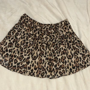 Leopardmönstrad kortkjol Gina Tricot - Supersnygg kortkjol från Gina Tricot med leopardmönster i beige, brunt och svart. Kjolen har en bred midja och lätt utställd form som ger en cool och trendig look. Perfekt för dig som vill sticka ut lite extra!