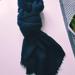 Svart lång halsduk i ull - Enkel och stilren svart halsduk i mjuk ull. Halsduken är lång och har lätt fransade kanter, perfekt att vira flera varv runt halsen. Passar dig som gillar en klassisk look med en touch av mysfaktor.  Små tråddragningar annars fint skick