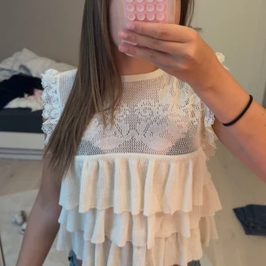 Vit volangblus med spets från Zara - Supersöt vit blus från Zara med flera lager volanger och detaljerad spets upptill. Ärmlös modell med spetskantade axlar och blommigt mönster i spetsen. Älskar denna men den kommer inte till användning längre tyvärr!! Verkligen super söt. Köpte för 399kr 