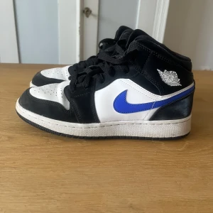 Nike Air Jordan 1 Mid svart/vit/blå - Nike Air Jordan 1 Mid sneakers med svart och vit ovandel i skinn och mocka, blå swoosh och klassisk Air Jordan-logga på sidan. Köpta för 1600 här på Plick därav inget kvitto och säljs för 350 + frakt eftersom de är använda och har några defekter. Pris går att diskutera😊
