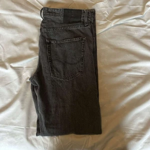 Svarta relaxed jeans Jack & Jones 32/34 - Säljer ett par mörk grå jeans från Jack & Jones i modellen Relaxed/Chris. Jeansen har en avslappnad passform, klassisk femficksdesign och raka ben. Tillverkade i bomull med snygg tvättad finish. Perfekta för en chill och stilren look.