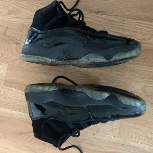 Svarta Nike Air Jordan 11 sneakers - Säljer ett par svarta Nike Air Jordan 11 med högt skaft och klassisk Jumpman-logga på hälen. Skorna har en blandning av blankt syntetmaterial och mockadetaljer, samt genomskinlig sula. Perfekta för dig som gillar ikoniska basketsneakers med cool design.