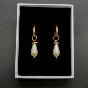 Guldiga örhängen med droppformad pärla - Snygga örhängen i guldton med droppformade vita pärlor som hänger från små ringar. Perfekt accessoar för att lyfta din stil med en elegant och trendig touch. Klassisk design med modern känsla, passar till många looks.
