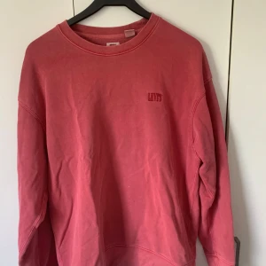 Röd/Rosa sweatshirt från Levi's i bomull - Säljer en relaxed fit sweatshirt från Levi's i en snygg rosa nyans. Tröjan har rund halsringning, långa ärmar och broderad Levi's-logga på bröstet. Tillverkad i mjuk bomull och passar perfekt för en chill och avslappnad stil.