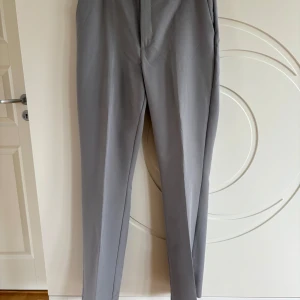 Grå kostymbyxor med raka ben - Snygga grå kostymbyxor med klassisk rak passform och pressveck. Byxorna har hällor för bälte. Perfekta för en clean och stilren look.