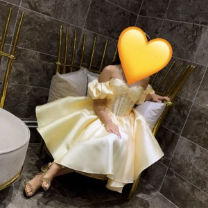 Champagnefärgad offshoulder kortklänning - Superfin champagnefärgad kortklänning med offshoulder och puffiga ärmar. Klänningen har en markerad midja med glittriga detaljer på livet och en voluminös kjol i satinliknande material. Perfekt för dig som vill sticka ut med en prinsessig look!