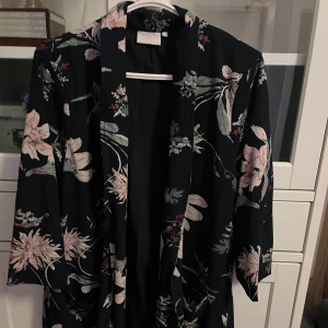 Blommig kappa från Kaffe,  - Säljer en svart kappa från Kaffe med blommiga mönster. Jackan har lös passform, trekvartsärmar. Storlek 40💕