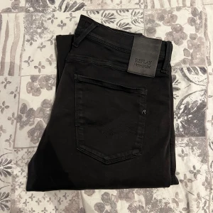 Replay Hyperflex Anbass jeans - Svarta Replay Hyperflex Anbass jeans med klassisk femficksdesign och snygga svarta detaljer. Jeansen är tillverkade i stretchigt material för extra komfort och har en slim passform. Perfekta för dig som gillar stilrena och bekväma jeans. Super fint skick på jeansen, inga defekter!