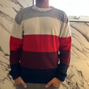 Randig tröja från GANT XL - Snygg randig tröja från GANT i storlek XL. Tröjan har breda blockränder i grått, vitt, rött, vinrött och mörkblått. Klassisk rund halsringning och långa ärmar. Perfekt för dig som gillar stilren och färgglad design.