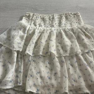 Vit blommig volangkjol från Vero Moda - Supersöt kort kjol från Vero Moda i vitt med små blå blommor.Ej använt så ofta. 🌸