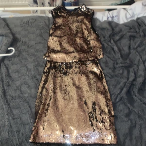 Guldig paljettklänning med svart insida - Snygg kort klänning täckt av guldiga paljetter med svart tyg på insidan. Ärmlös modell med rund halsringning och rak passform. Perfekt för dig som vill sticka ut med glitter och glam på festen! Och får ursäkta bilderna min kamera är lite sönder så men försökte iallafall. Och vi kan prata om priset om det behövs! 