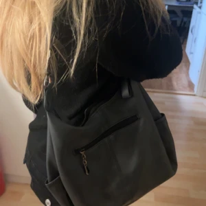 Svart axelväska  - Snygg svart axelväska med flera praktiska fack och dragkedjor framtill. Väskan har en stilren design med bred axelrem och silverfärgade metalldetaljer. Perfekt storlek för att få plats med allt du behöver till skolan eller stan.