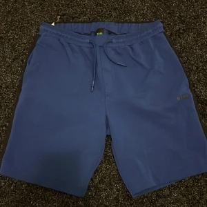 Blå shorts från BOSS med snörning - Snygga blå shorts från BOSS med elastisk midja och snörning för perfekt passform. Stilren design med diskret BOSS-logga på benet. Perfekta för sommaren och chill dagar.