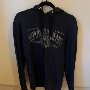 Mörkblå hoodie från Replay Blue Jeans - Snygg mörkblå hoodie från Replay Blue Jeans med tryck framtill och justerbar snörning i huvan. Tröjan har långa ärmar och ribbade muddar. Perfekt för en chill och avslappnad stil.