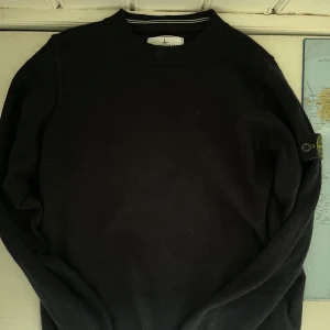 Svart stickad tröja Stone Island Junior - Svart stickad tröja från Stone Island Junior med klassisk crewneck. Tröjan är gjord i ull och i bra skick förutom 2 väldigt små hål på vänster arm. går säkert att fixa hos skräddare! Tröjan är också självklart äkta.
