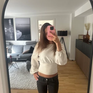 Vit ribbad blus med ballongärmar - Supersnygg vit blus med ribbat tyg och bred midjeresår. Ballongärmar med diskreta puffar och rund halsringning. Perfekt till jeans eller kjol för en trendig stil. Köpt på hm för länge sedan och finns ej kvar. 