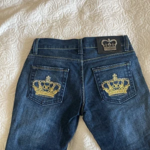 Victoria Beckham - Snygga mörkblåa lågmidjade jeans från Victoria Beckham, med snygga guldiga kronor på bakfickorna. Storlek W28 L32