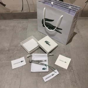 Lacoste Metropole silverfärgad klocka - Stilren klocka från Lacoste i silverfärgat rostfritt stål med länkarmband och diskret Lacoste-logga. Klockan har en modern, rektangulär design och levereras med originalförpackning, påse och certifikat. Perfekt accessoar för dig som gillar klassisk men trendig stil.