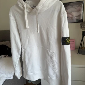 Stone Island vit hoodie strlk S - Vit hoodie från Stone Island med klassisk patch på vänster ärm. Tröjan har huva med snörning och en stor magficka. Tillverkad i mjuk bomull, perfekt för en clean och stilren look. Långärmad och normal passform. 