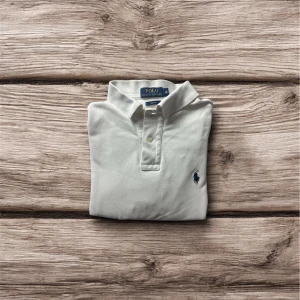 Vit Ralph Lauren Piké - ✔ Färg: Vit ✔ Storlek: M (Slim Fit – kroppsnära modell) ✔ Modell: Herr ✔ Material: 100% bomull ✔ Skick: Mycket bra – med ett litet hål på baksidan som knappt syns  📌 Det finns ett superlitet hål på ryggen (se bild vid behov) men det påverkar inte passformen eller helhetsintrycket – det är inget man märker när den bärs.  Det här är en klassiker i garderoben som alltid går att lita på – oavsett om du klär upp dig eller ned dig.  📦 Skickas snabbt eller kan mötas upp 📩 Skriv om du vill ha fler bilde