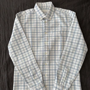 Rutig skjort-jacka från Casual Friday - Snygg rutig skjorta från Casual Friday i vitt och ljusblått. Skjortan har klassisk krage, knäppning framtill och en bröstficka. Tillverkad i mjuk bomull med lång ärm och relaxed vibe. Perfekt för dig som gillar stilren men clean look.