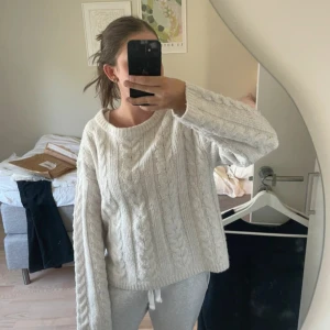 Vit kabelstickad tröja - Mysig vit kabelstickad tröja med rund hals och lång ärm. Tröjan har en loose passform och är perfekt för kyliga dagar. Den stickade strukturen ger en klassisk och trendig look som funkar till allt.