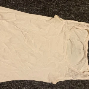 Vit ribbad linnetopp med spetsdetalj - Säljer en söt vit ribbad linnetopp från Dolce med fina spetsdetaljer vid axlarna. Toppen är ärmlös och har en rund halsringning. Perfekt för att styla lager på lager eller bära som den är under varma dagar.