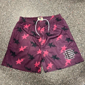 Lila meshshorts från Eric Emanuel - Snygga lila meshshorts från Eric Emanuel med rosa och svarta stjärnor över hela tyget. Shortsen har elastisk midja med vit snörning och en stor EE-logga på ena benet. Perfekta för dig som vill sticka ut med ett coolt mönster och sportig vibe.