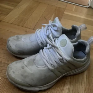 Vita Nike Presto sneakers - Snygga vita Nike Presto sneakers med klassisk mesh-ovandel och bred snörning. Skorna har en mjuk, vadderad insida och en flexibel sula för extra komfort. Ikonisk Nike-logga på sidan och tå, samt transparenta detaljer på sidorna.