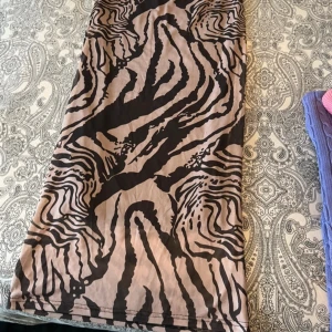 Beige långkjol med zebramönster - Cool långkjol i beige med svart zebramönster. Kjolen har en rak passform och är perfekt för dig som vill sticka ut med ett djurmönster. Materialet känns mjukt och följsamt, vilket gör den skön att bära hela dagen.