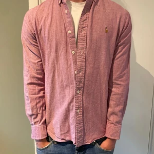 Rosa skjorta från Ralph Lauren S - Säljer en snygg rosa skjorta från Ralph Lauren i slim fit-modell. Skjortan är i stretchig bomull, har klassisk krage, knappar framtill och broderad logga på bröstet. Perfekt till jeans eller chinos för en clean look.