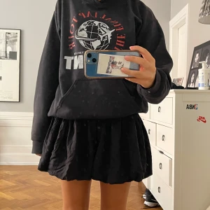 Svart kortkjol med smock i midjan - Supersöt svart kortkjol med bred smock i midjan och voluminös, lätt utställd form. Kjolen är enkel och stilren, perfekt att matcha med hoodies eller crop tops. Tillverkad i mjukt tyg som känns skönt mot huden.