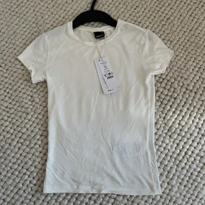 Vit tight t-shirt från Gina Tricot - Säljer en basic vit t-shirt från Gina Tricot. Modellen är tight och har korta ärmar samt rund halsringning. Perfekt att styla med jeans eller kjol. Materialet är mjukt och stretchigt, vilket gör den riktigt skön att bära.