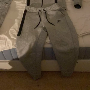 Grå Nike tech, storlek M - Säljer en ”Nike tech tracksuit” med både byxorna och hoodien i storlek M. Perfekta för chill eller träning, med skön passform och elastisk midja. Är själv medium och är lite stor på mig men passar enda bra. Skicket är så gott som nytt. Priset är ej hugget i sten🤑. Kontakta vid frågor och intresse😁👌
