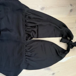 Svart halterneck topp från Gina Tricot - Snygg svart halterneck topp från Gina Tricot i mjuk polyester. Toppen har knyt i nacken och en lätt rynkad söm under bysten som ger en cool och trendig look. Perfekt att styla med jeans eller kjol för en chic vibe.