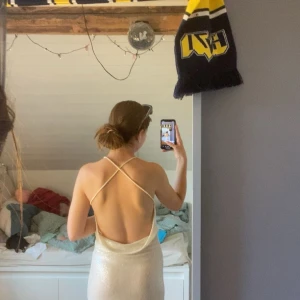 Glittrig långklänning DK Valencia S - Supersnygg glittrig långklänning från DK Valencia i ljus champagnefärg. Klänningen har smala axelband som korsas i ryggen och en öppen rygg. Materialet är glittrigt och faller snyggt längs kroppen. Perfekt för bal eller student! Pris kan sänkas!