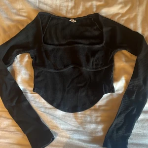 Svart ribbad långärmad topp - Säljer en svart ribbad långärmad topp från Nelly med fyrkantig urringning och markerad söm under bysten. Toppen är croppad och har en tight passform.