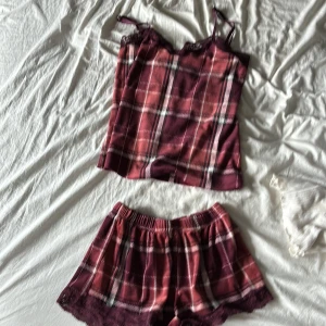 Rutig pyjamasshorts från Hunkemöller - Mysiga rutig pyjamasshorts från Hunkemöller i vinröda och rosa toner med spetsdetaljer längst ner. Mjukt material och elastisk midja för extra komfort. Perfekta för chillkvällar hemma.