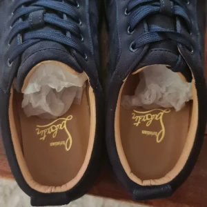 Svarta sneakers från Brishan - Snygga svarta sneakers från Brishan med klassisk snörning och kontrasterande röd sula. Ovandelen är i textil med diskret broderad logga på hälen och insidan har en beige innersula med gul logotyp. Perfekta för dig som gillar stilrena och unika detaljer.