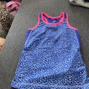Blå leopardmönstrad linnetopp H&M - Sportig linnetopp från H&M med blått leopardmönster och kontrasterande rosa kantband. Toppen är ärmlös och har en tight passform, perfekt för träning eller aktiva dagar. Tillverkad i mjuk och stretchig polyester som andas.