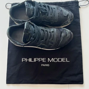 Svarta sneakers från Philippe Model - Snygga svarta sneakers från Philippe Model Paris med coola detaljer och mix av material. Skorna har snörning, rund tå och vit sula. Perfekta för dig som gillar en urban och trendig stil. Kommer med originalpåse.