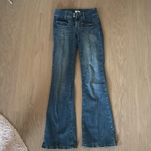 Nelly jeans( blå bootcut jeans/ lowaist ) - Snygga blå jeans med bootcut-modell och markerade sömmar längs benen. Framtill finns två stora fickor med lock och dubbla knappar i midjan. Jeansen har en klassisk tvätt och är tillverkade i jeansmaterial med lite stretch. Jeansen är ifrån Nelly. Har används mindre än 10 gånger. 