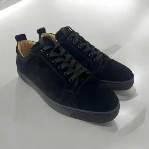 Svarta skor från Louboutin - Stilrena svarta sneakers från Christian Louboutin i mjuk mocka med svarta snören och diskreta sömmar. Skorna har rund tå, platt sula och beige innersida. Perfekta för dig som gillar lyxiga detaljer och klassisk design.