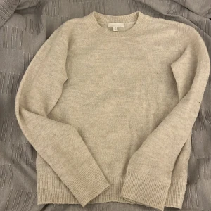 Beige stickad tröja - Mysig beige stickad tröja med rund hals och långa ärmar. Perfekt för kyliga dagar och enkel att matcha med olika outfits.