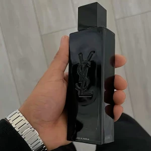 YSL svart parfymflaska - Snygg parfym från Yves Saint Laurent i en stilren, svart och glansig rektangulär flaska med YSL-loggan i relief på framsidan. Flaskan har en modern och lyxig känsla med en fyrkantig svart kork. Perfekt för dig som gillar exklusiva dofter.