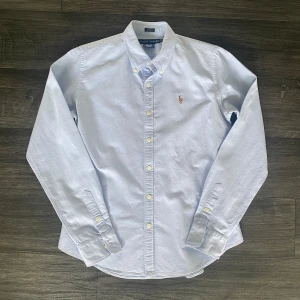 Ljusblå skjorta från Ralph Lauren - Klassisk ljusblå skjorta från Ralph Lauren i slim fit-modell. Skjortan är tillverkad i 100% bomull. Den är i storlek 10 den är 70cm lång och har en axelbred på 38cm dem borde passa som en s men kan va skillnad. Om du har frågor kring plagget är det bara att skriva mvh FABIANFASHION 